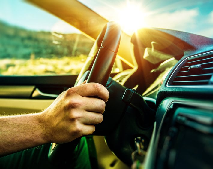 Man's hands on steering wheel, driving with summer sun streaming through window