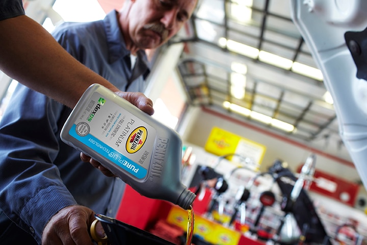 Firestone Complete Auto Care technician pouring Pennzoil Platinum oil into engine