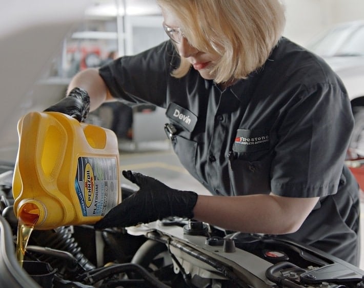 Firestone mechanic pouring Pennzoil motor oil into an engine