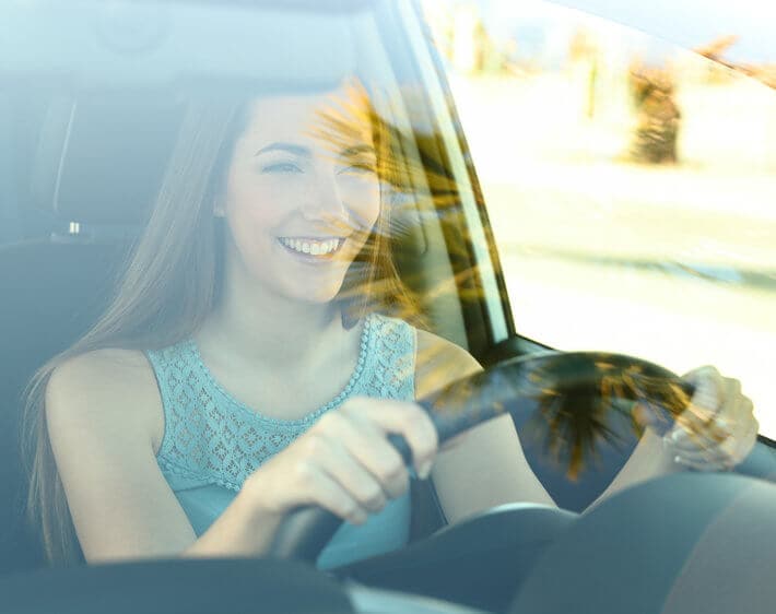 woman driving car smiling through windshield reflection