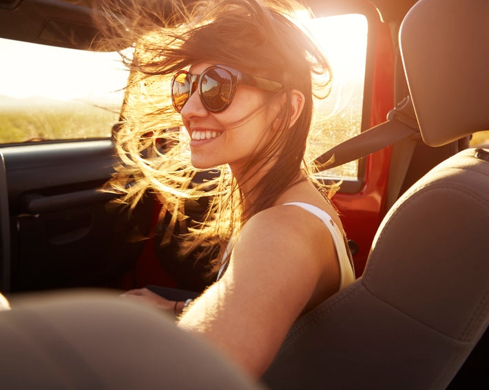 Woman passenger on road trip, riding in red convertible as sun sets